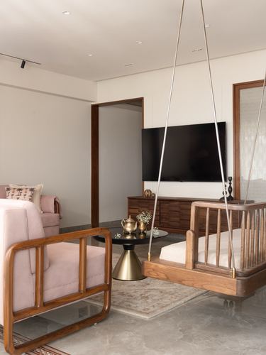 Living room with wooden hanging swing, pink armchair, black-brass coffee table, wall-mounted TV