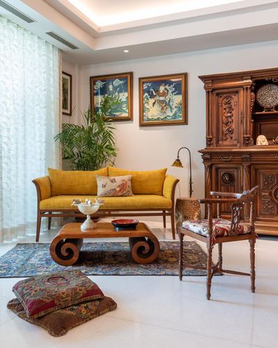 Living room with mustard sofa, carved wooden cabinet, thangka paintings and scroll coffee table