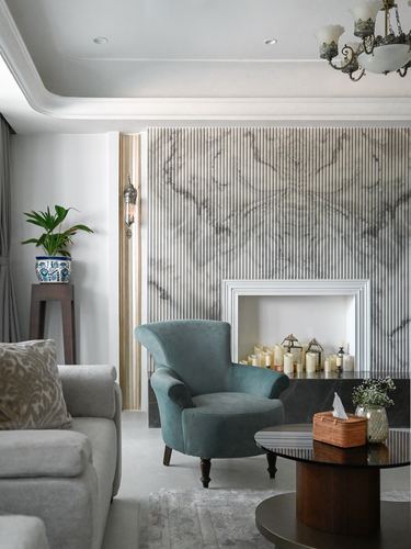 Living room with teal velvet armchair before a fluted-panel fireplace wall and chandelier above