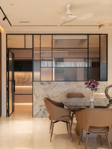 Dining area with marble-topped table, tan leather chairs, and a black-framed glass partition to a kitchen beyond