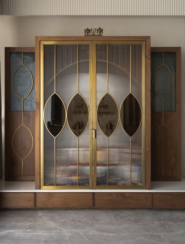 Wooden pooja unit with brass-framed glass doors and lotus motifs, backlit interior