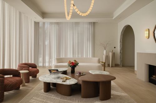 Living room with sheer curtains, rust armchairs, marble-topped wood coffee tables, arched doorway
