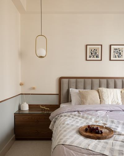 Bedroom corner with channel-tufted headboard, wooden nightstand, brass pendant light and wine tray on bed