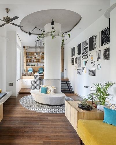 Bright living room with curved grey sofa around white column, gallery wall, wood flooring and yellow bench