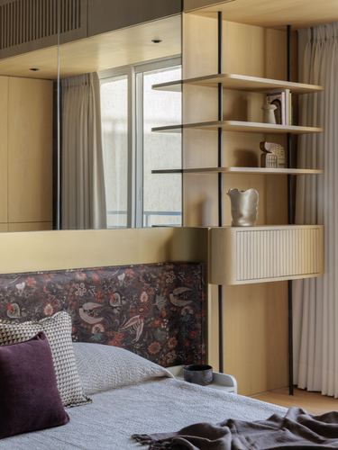 Bedroom corner with floating wood shelves, mirror panel, and floral upholstered headboard