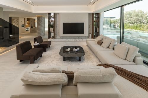 Contemporary living room with marble tv wall, dark armchairs, and sliding glass doors opening to a pool