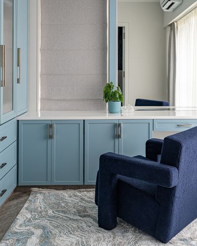 Powder blue built-in cabinetry with white countertop and navy bouclé armchair in study nook