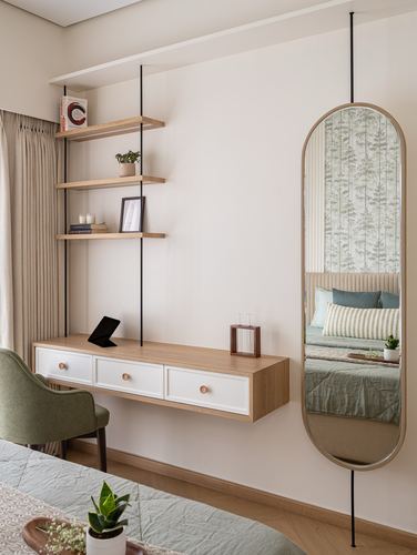 Bedroom vanity nook with floating wood shelves, drawer console, and tall oval mirror reflecting bed
