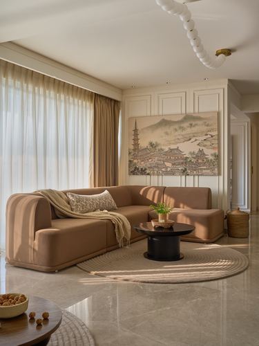 Curved camel sofa facing round black coffee table in sunlit marble-floored living room