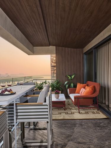 Terrace lounge with orange wicker sofa, dining table, and jali screen overlooking a river at sunset