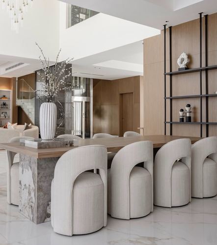 Open dining area with barrel-back chairs around a stone-based table beneath a double-height ceiling