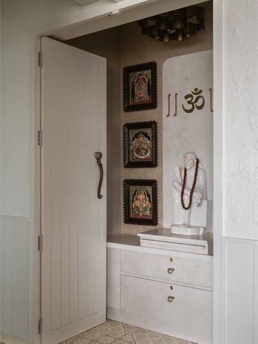 Pooja niche with framed deity paintings, white statue, and brass pendant light beside an open door