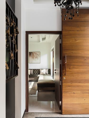 Entry foyer with wooden pivot door opening to a view of a tufted sofa living room