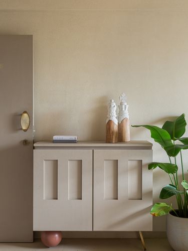 Beige textured wall with cream cabinet, wood and ceramic bottles, brass sconce, and potted plant