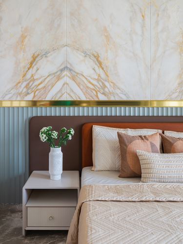 Bedroom corner with book-matched marble wall, brass trim, fluted sage headboard wall, and layered cushions