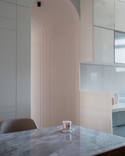 Marble dining table with teacup beside an arched pastel pink niche leading to kitchen