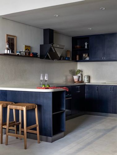 Dark blue L-shaped kitchen with pale stone island counter and cane bar stools
