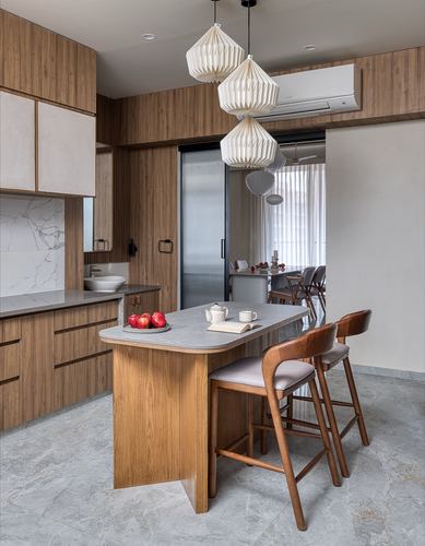 Wood-panelled kitchen with island, paper pendant lights, and stone flooring in Japandi-style home