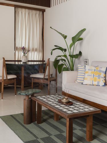 Living room corner with wood-framed sofa, tiled coffee table, stone side table, and large banana plant