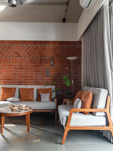 Living room with herringbone brick wall, wooden armchair and sofa with rust cushions