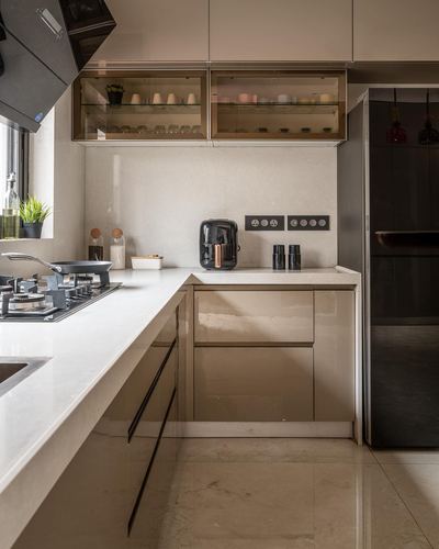 L-shaped modern kitchen with glossy taupe cabinets, glass upper units, and stone countertop