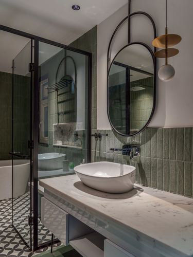 Bathroom with green tiled walls, marble vanity, vessel sink, oval mirrors and glass shower partition