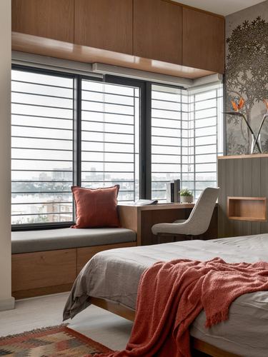Bedroom window seat with desk beside city-view windows, bed with terracotta throw in foreground