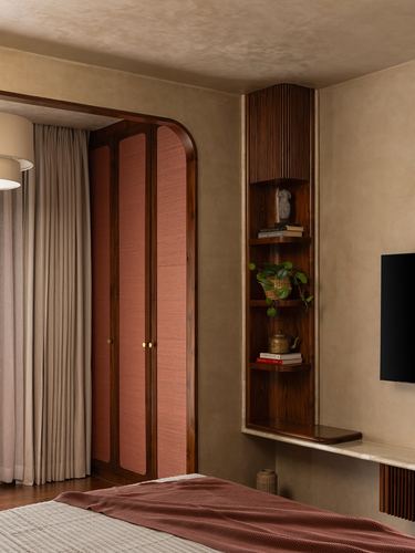 Arched wardrobe with terracotta panels beside a fluted wooden corner shelf in a warm-toned bedroom