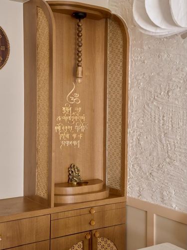 Arched wooden pooja unit with cane panels, brass Ganesha idol, and textured plaster wall beside it