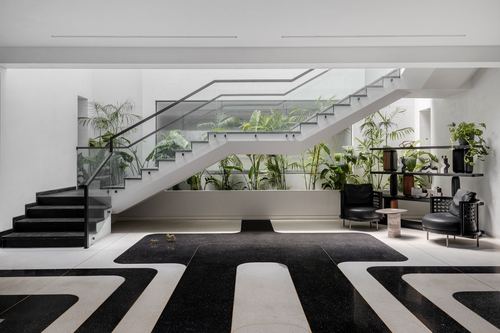 Black and white terrazzo foyer with floating staircase and glass balustrade over lush planting