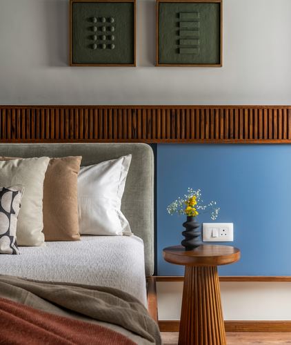 Bedroom corner with slatted wood headboard trim, blue accent panel, fluted wood side table and vase