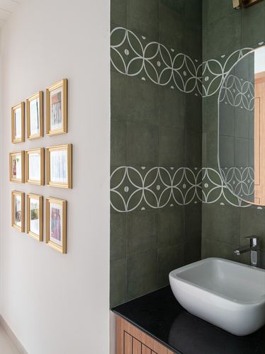 Powder room with green patterned tile, vessel sink, black counter, and gold-framed photo gallery on white wall