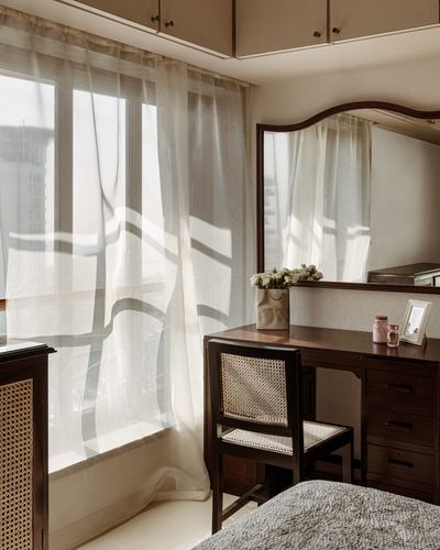 Dressing table with mirror and cane chair beside sunlit sheer curtains in bedroom