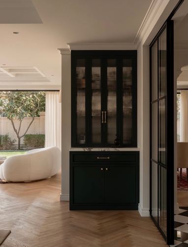 Dark green glass-front cabinet in white archway beside herringbone floor and curved sofa
