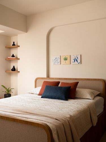 Beige bedroom with wood-framed bed, terracotta and navy cushions, arched wall niche and floating corner shelves
