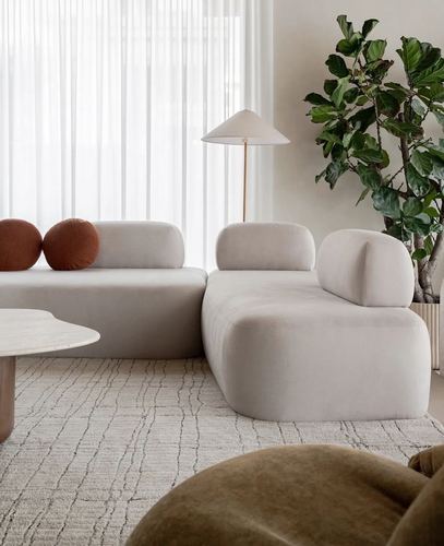 Curved beige sectional sofa with terracotta round pillows beside a stone coffee table and floor plant