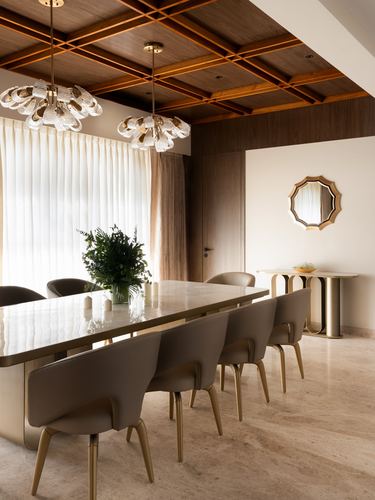 Dining room with marble-look table, brass-legged chairs, and coffered wood ceiling with chandeliers