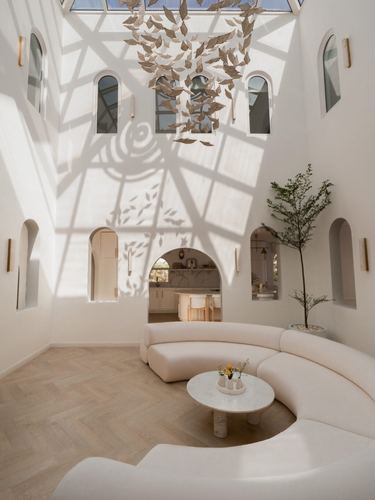 Double-height white living room with arched niches, curved sofa, and skylight casting leaf-shaped shadows