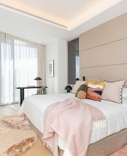 Bedroom with tufted taupe headboard, white bedding, pink throw, and sheer curtains