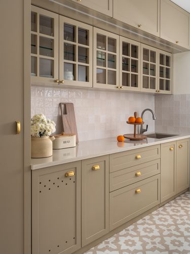 Taupe kitchen with glass cabinets, brass handles, patterned floor tiles and oranges on counter