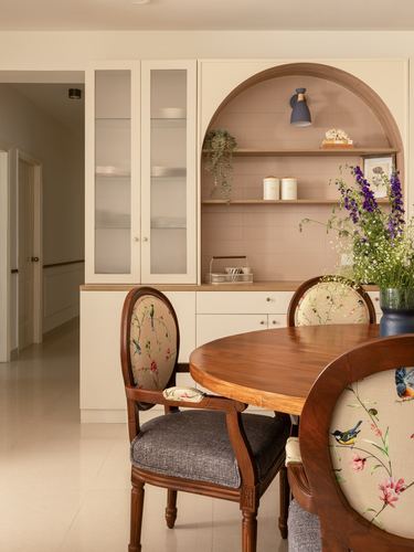 Dining area with arched fluted niche, cream cabinetry, and floral cane-back chairs around wooden table