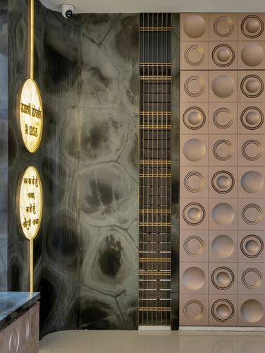 Entrance wall with veined dark stone, glowing nameplate ovals, brass grille, and pink relief-tiled panel