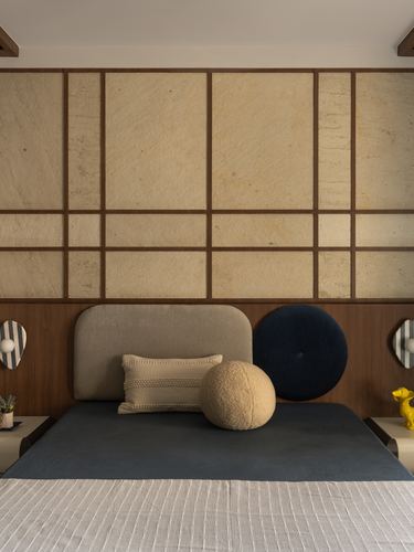 Bed with grey curved headboard and navy circular cushion against a gridded stone and wood panel wall