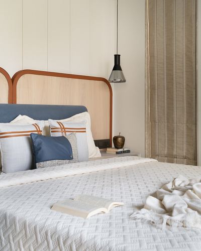Bed with arched wood headboard, blue and cream pillows, and a black pendant light beside striped curtains
