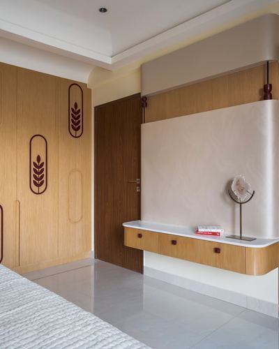 Bedroom corner with curved floating console and wheat-motif wardrobe panelling in Chennai apartment