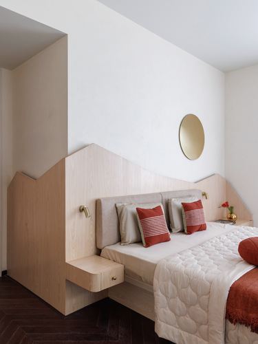 Bedroom with zigzag wood headboard, built-in nightstands, round brass mirror, and terracotta cushions