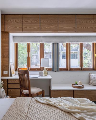 Bedroom with wooden desk, chair and window seat beneath a long window wall