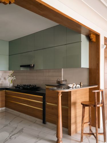 Kitchen with sage green upper cabinets, wood lower cabinets with brass trim, and a turned wood pillar peninsula