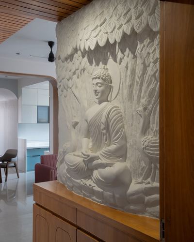 Sculpted white plaster relief of seated Buddha above a wooden sideboard in a hallway
