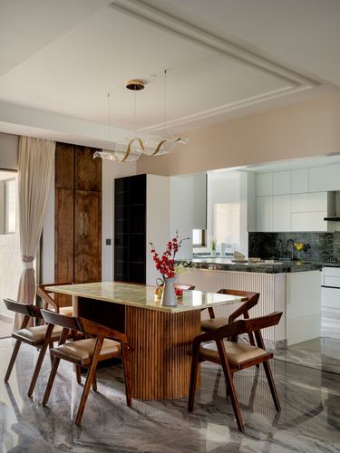 Dining table with fluted wood base and marble top under sculptural pendant light, kitchen visible beyond